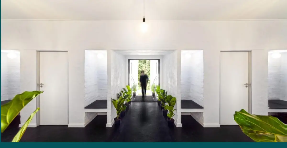 A light-filled corridor at an Epione Health Village, with white walls, black flooring and potted plants leading to an entrance.
